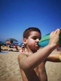 Shirtless boy drinking water at beach against sky