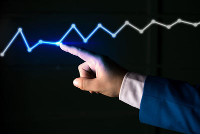 Midsection of man touching illuminated light against black background