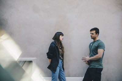 Male and female computer programmers discussing against wall in office