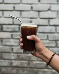 Cropped hand holding drink against brick wall