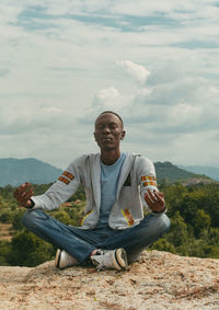 Mid adult man meditating while sitting on mountain against sky