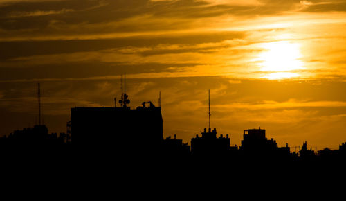 Silhouette of city against cloudy sky during sunset