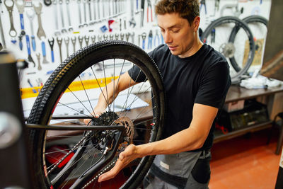 Male technician attaching wheel to bike while working in professional modern workshop