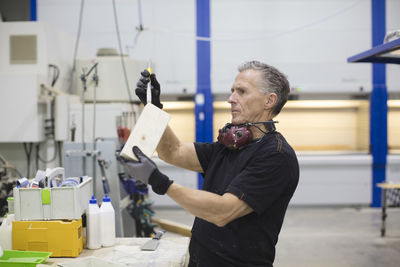 Senior worker painting wooden box while standing in industry