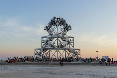 People at amusement park ride against sky during sunset