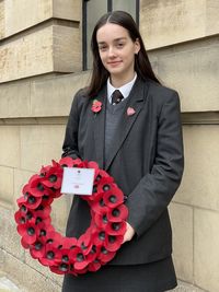 Sixth form girl student in school uniform with poppy wreath to lay at remembrance sunday service 