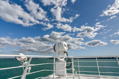 Searchlight on railing by sea against sky