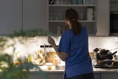 Rear view of nurse removing glassware from cabinet in kitchen at home