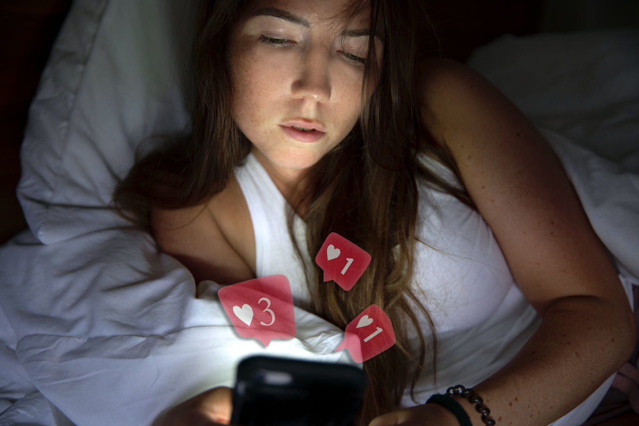 MIDSECTION OF WOMAN USING SMART PHONE WHILE STANDING ON BED