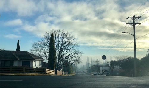 Road amidst trees and buildings against sky