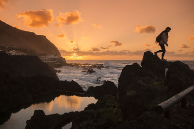 Silhouette man on rock by sea against sky during sunset