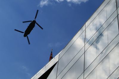 Low angle view of military helicopter over building against sky