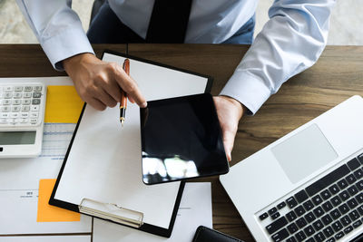 Midsection of businessman using digital tablet while sitting at desk in office