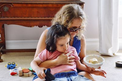 Grandmother feeding granddaughter while sitting at home