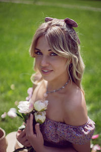 Portrait of a beautiful young woman sitting on a green meadow in summer and holding a bouquet 