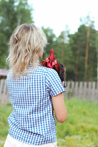 Rear view of woman with rooster on the farm