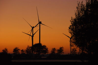 Silhouette of wind turbines on field against romantic sky
