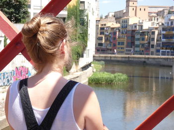 Rear view of woman standing on bridge against river in city