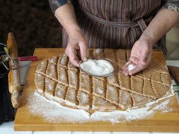  an elderly woman's hands sprinkle sugar on sliced raw biscuits for baking in the oven.