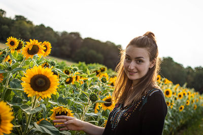 Portrait of smiling woman with sunflower against sky