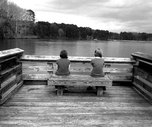 Rear view of siblings sitting on pier in front of lake