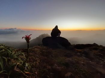 Silhouette of man sitting on rock against sky during sunset