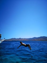 Man surfing in sea against clear blue sky