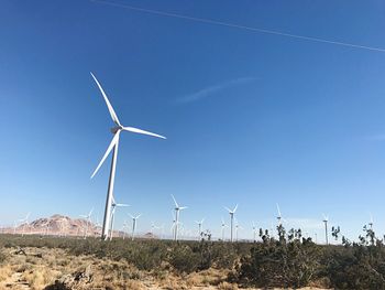 Wind turbines on landscape against blue sky