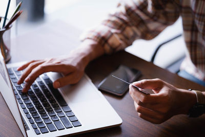 Midsection of man holding credit card and using laptop on table 