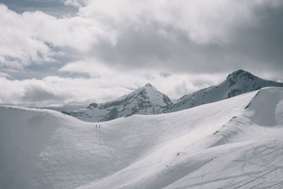 Two unrecognisable backcountry skiers at ridge against snowcapped peak