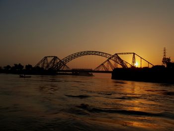 Silhouette bridge over river against sky at sunset