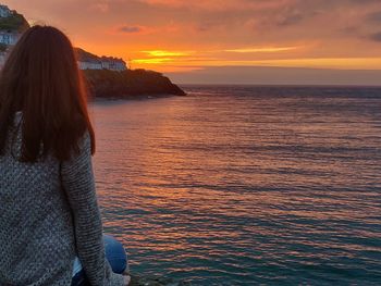 Rear view of woman looking at sea against sky during sunset