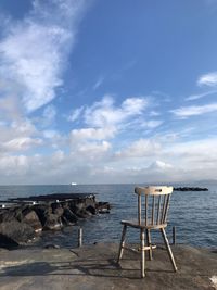 Deck chairs on rocks by sea against sky
