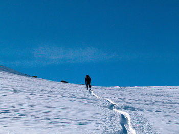 Person on snowcapped mountain against blue sky