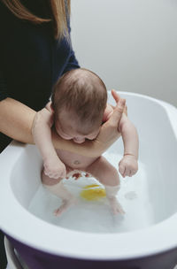 Midsection of mother bathing son in bathtub at bathroom