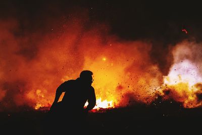 Silhouette man standing against fire at night