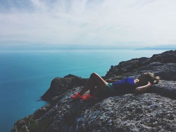 Young woman lying on rock in sea against sky