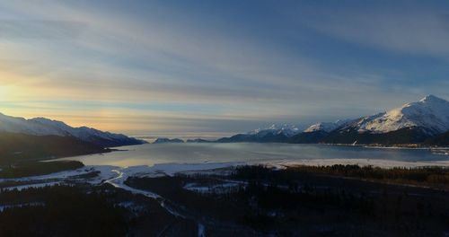 Scenic view of lake by snowcapped mountains against sky during sunset