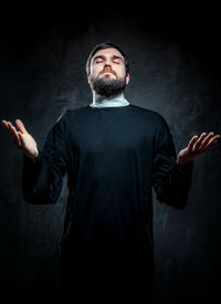 Priest with eyes closed standing against black background