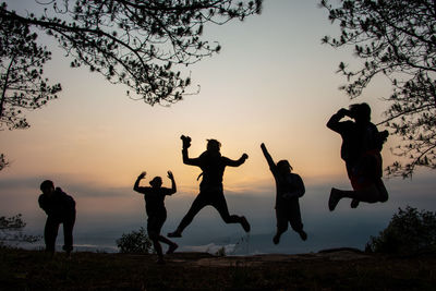 Silhouette friends jumping on top of mountain against sky during sunset