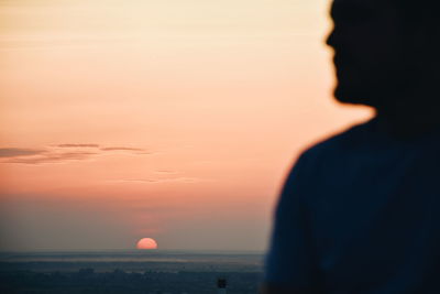 Silhouette man standing on rooftop against sky during sunset