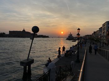 People by sea against sky during sunset