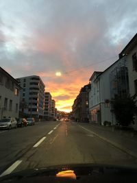 Road amidst buildings against sky during sunset