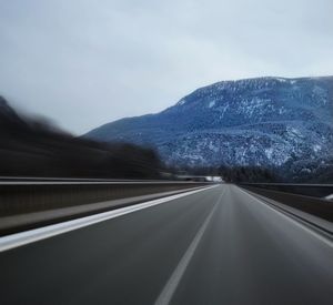 Road by snowcapped mountains against sky