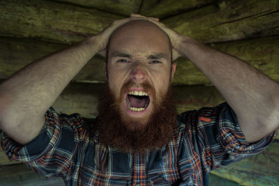 Close-up portrait of frustrated bald man screaming in log cabin