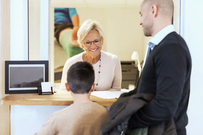 Smiling female receptionist attending family at counter in orthopedic clinic