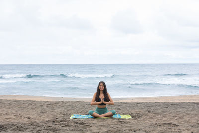 Fit young woman practicing yoga on sandy seashore