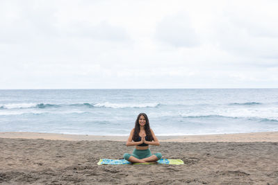 Rear view of woman sitting at beach against sky