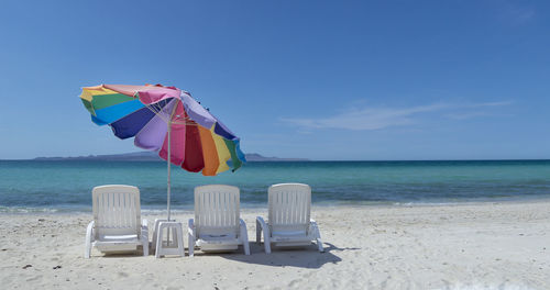Empty lounge chairs and umbrella at beach against blue sky