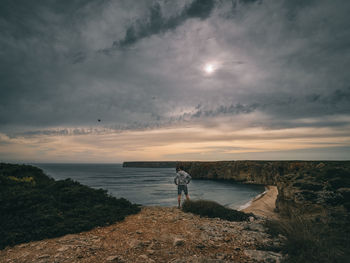 Rear view of man standing by sea against sky during sunset